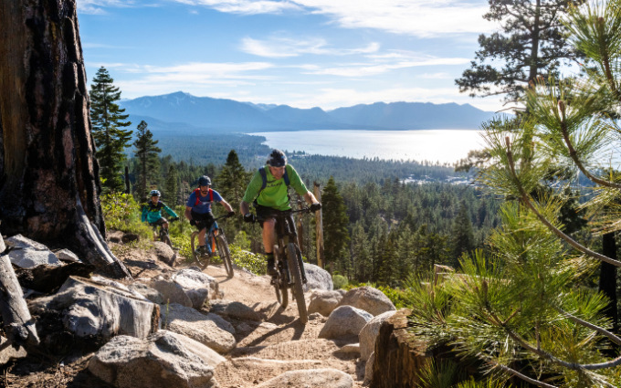 Three bikers on a mountain trail above a lake