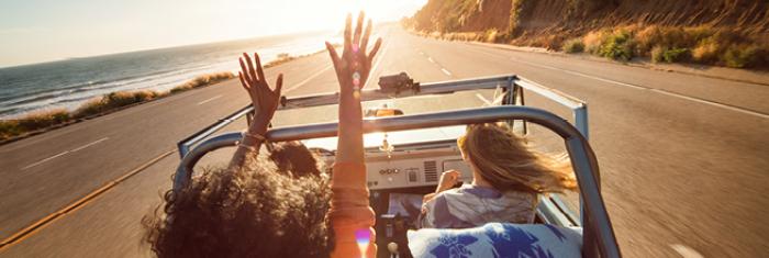 People in a convertible on a highway by a coastline